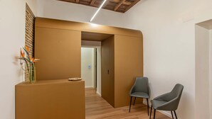 A modern interior with a reception desk, two grey chairs, wooden flooring, and a wooden ceiling. - Ora Acanfora Suites (Rome)
