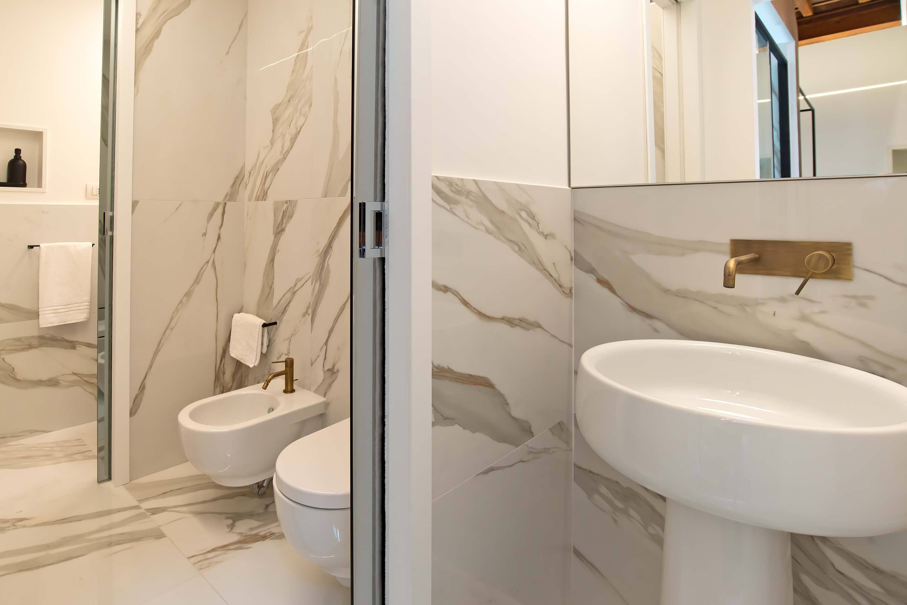 A modern bathroom with a bidet, toilet, and sink, all with marble-like tile walls and floors.