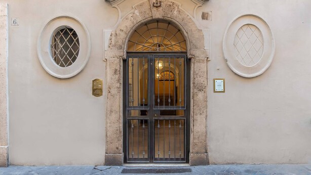 A building entrance with a large arched doorway, two round windows, and a number plaque. - Ora Acanfora Suites (Rome)