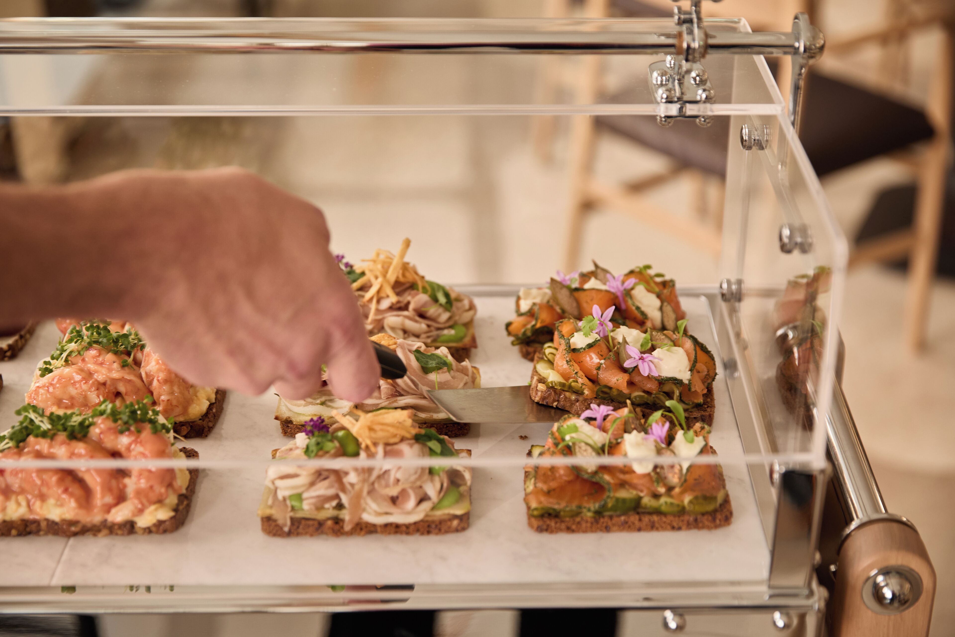 A food display with various sandwiches and a hand placing a sandwich on the board.