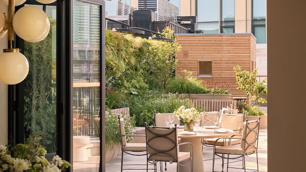 Een modern buitenDining gebied met een ronde tafel en stoelen, omgeven door weelderig groen en uitzicht op de stad.