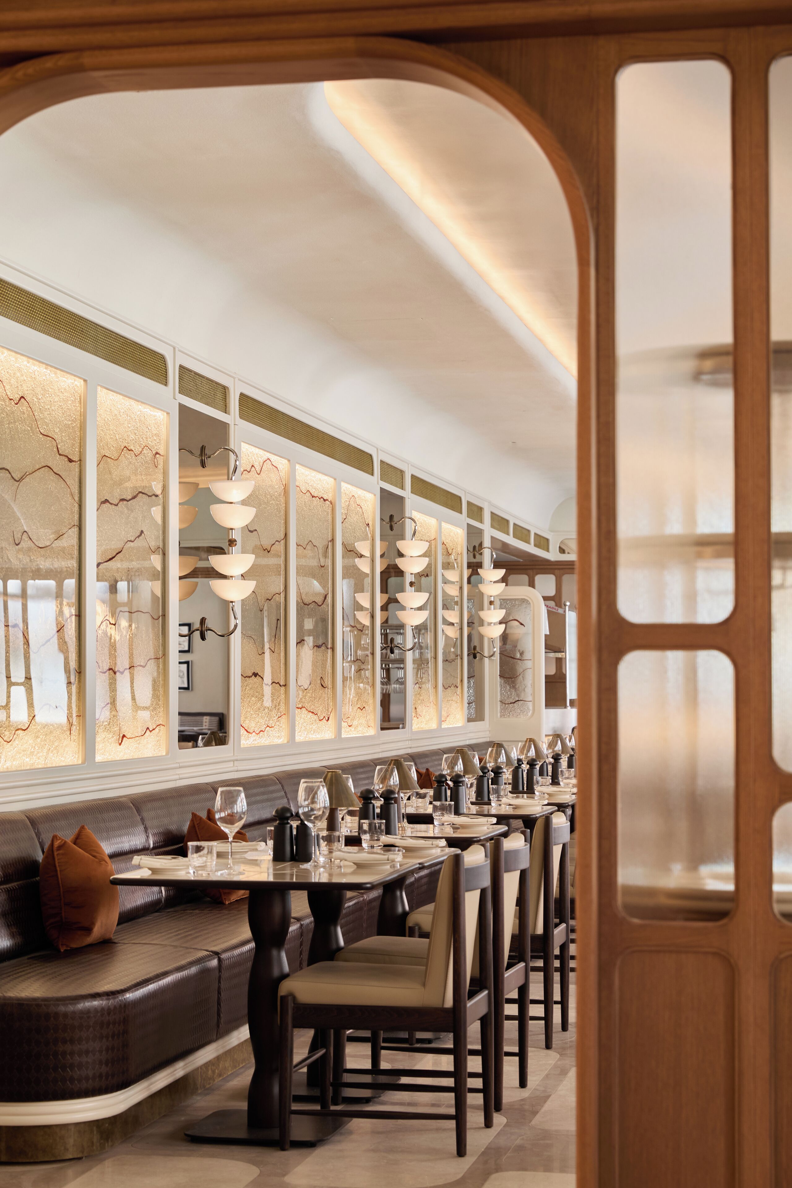 A modern dining area with a long table, cushioned seating, and decorative lighting.