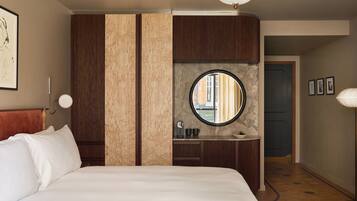 A hotel room with a large bed, a round mirror, a small sink, and a wardrobe.
