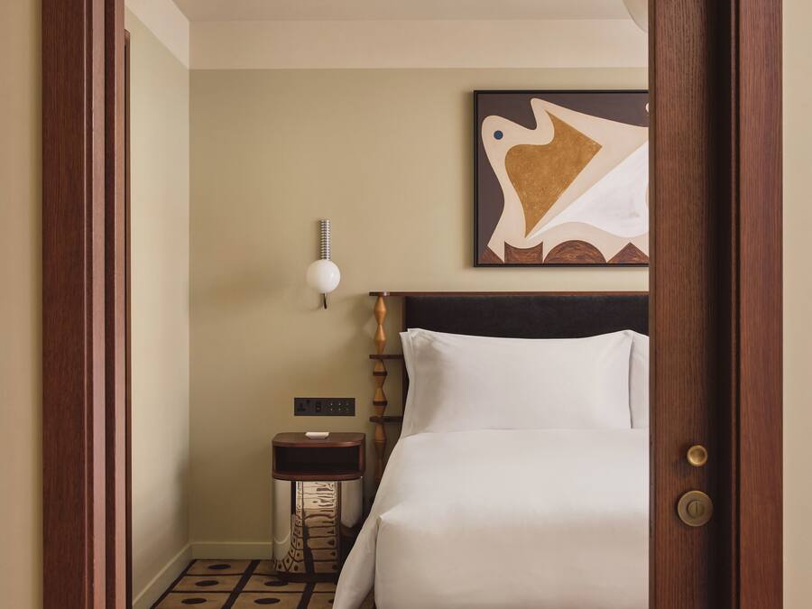 A hotel room with a bed, a nightstand, a wall-mounted lamp, and a painting.