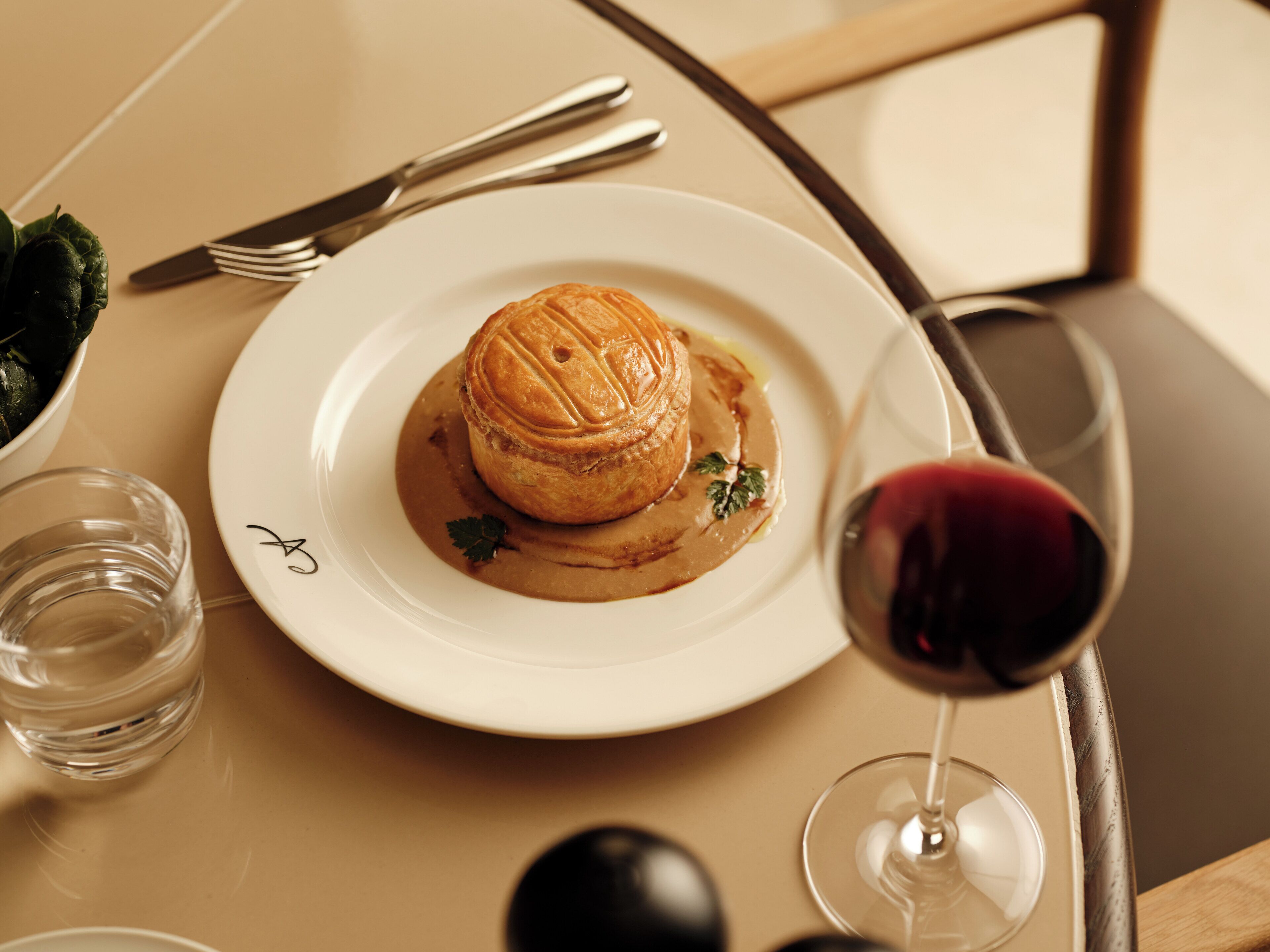A plate with a pastry, a glass of red wine, and cutlery on a table.