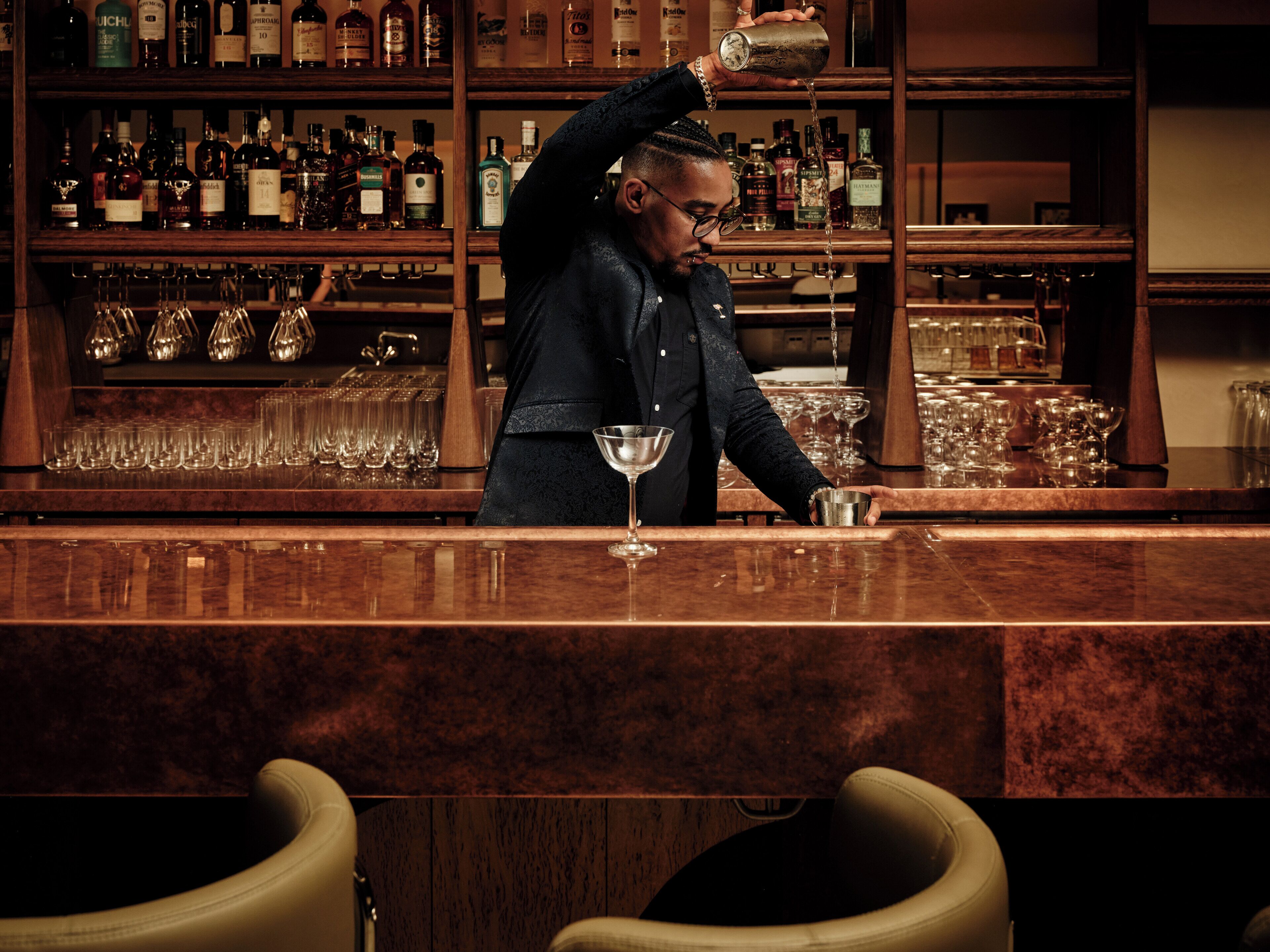 Un bar où un barman verse une boisson dans un verre à martini.