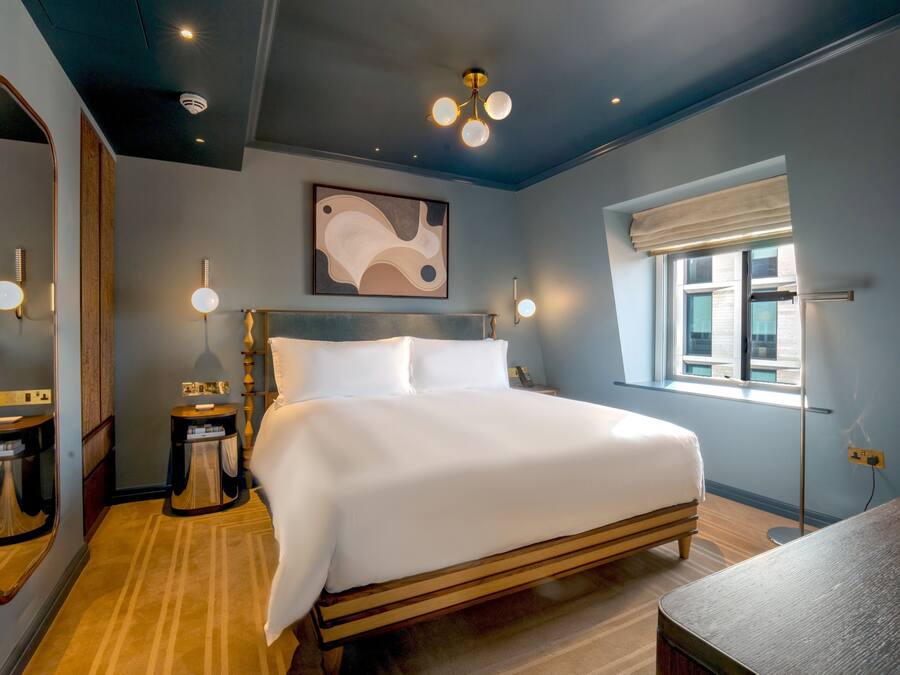 Une chambre à coucher avec un grand lit, une table de chevet, un miroir, une fenêtre donnant sur un beau paysage et un luminaire au plafond.