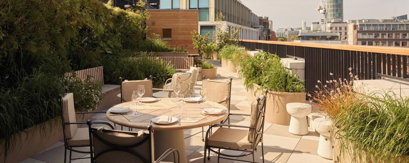A rooftop terrace with round tables, chairs, and potted plants.