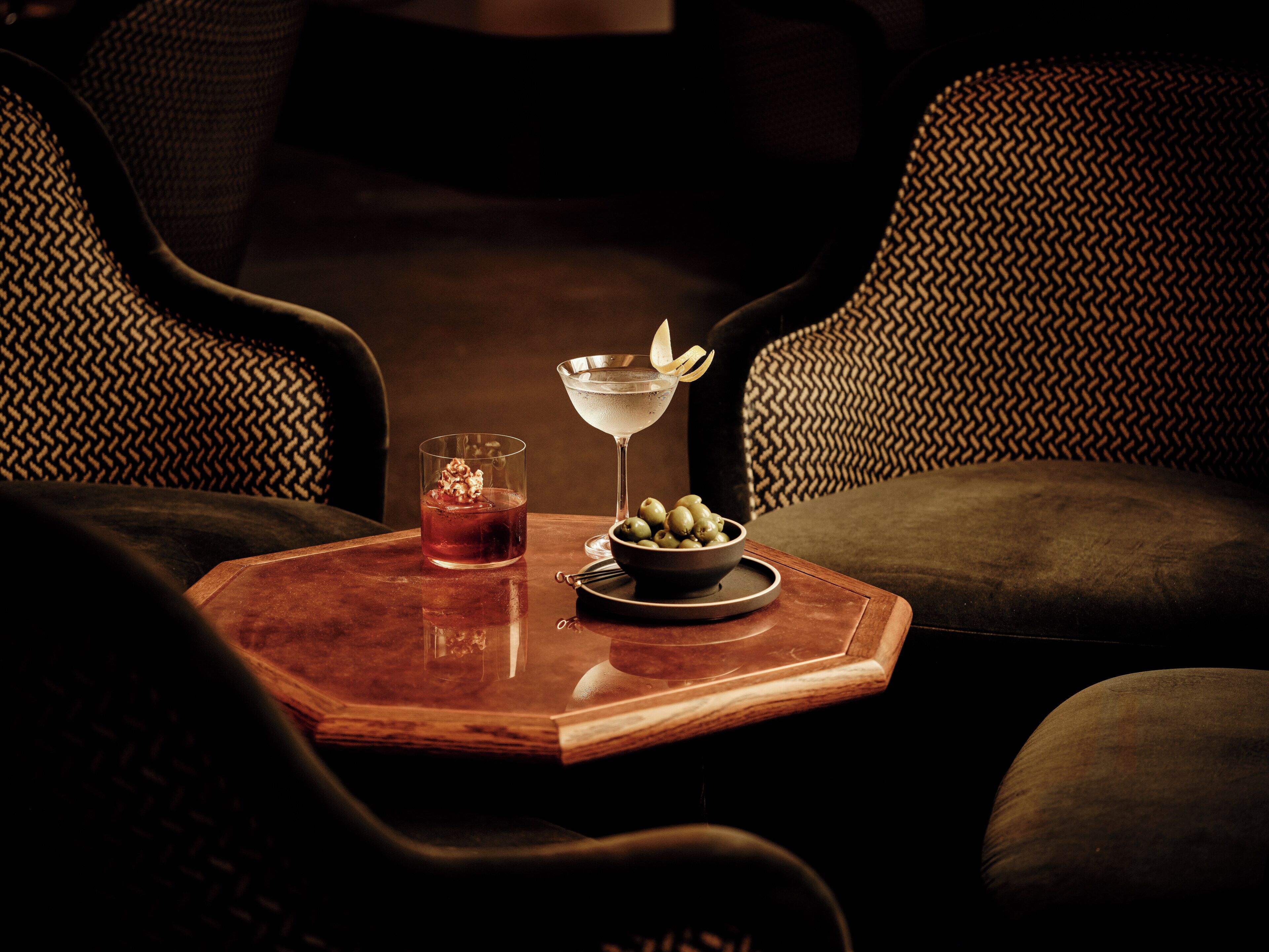 Uma mesa de madeira com uma taça de martini e uma travessa de azeitonas.