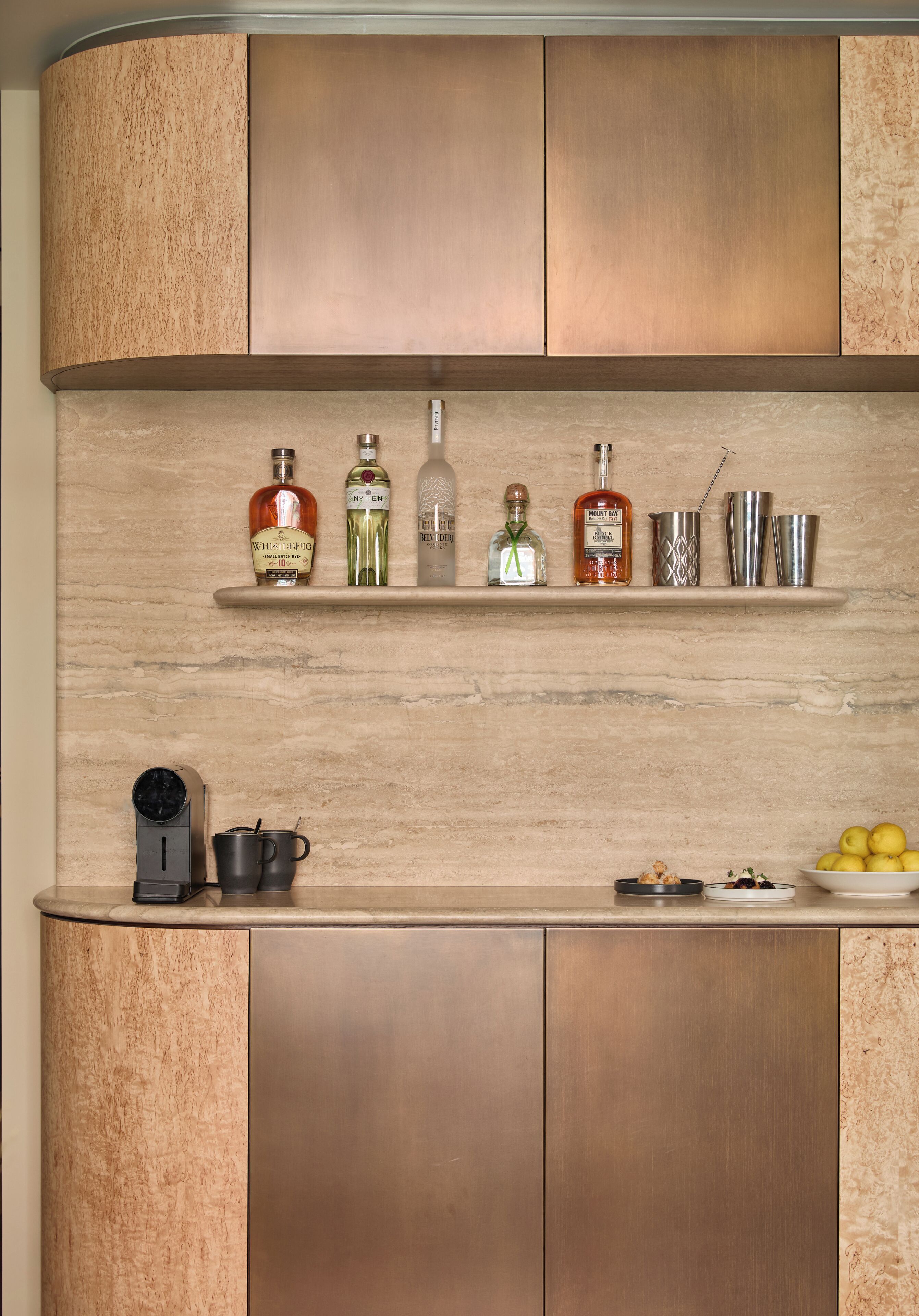 Una cocina con armarios de madera, una encimera y diversos objetos, incluyendo botellas y una cafetera.