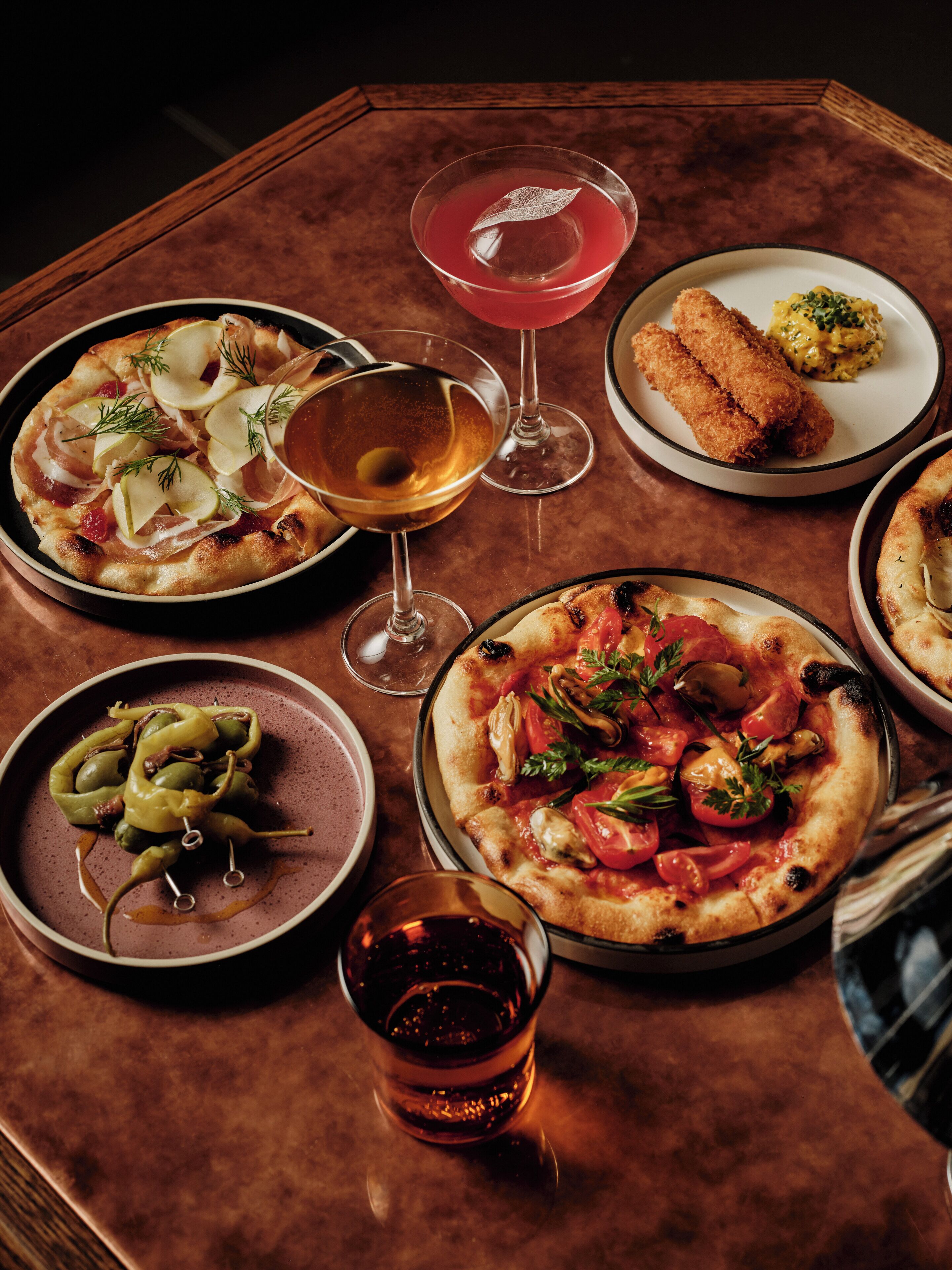 Une table dressée avec divers plats, notamment des pizzas et un verre à martini.