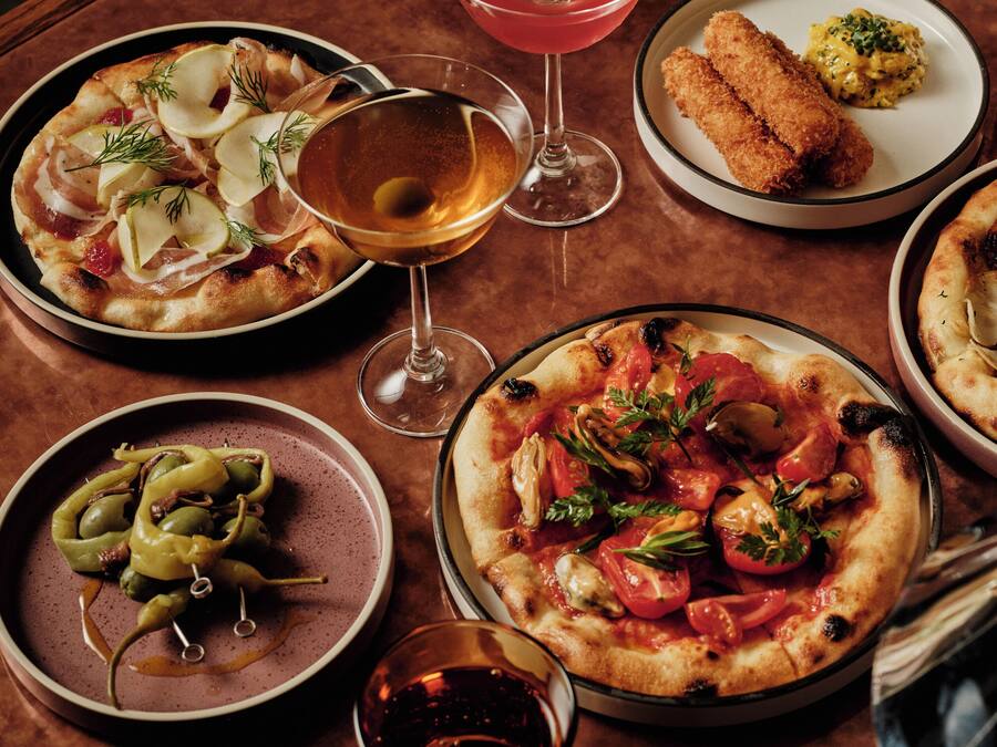 Une table dressée avec divers plats, notamment des pizzas et un verre à martini.