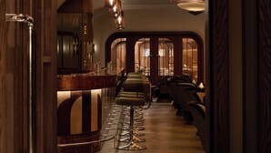 A corridor with a bar area, seating, and a ceiling with a geometric light fixture. - The Newman (London)