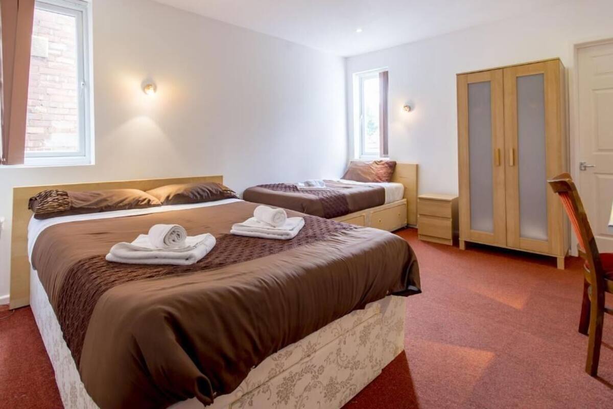 A hotel room with two beds, a wardrobe, and a chair.