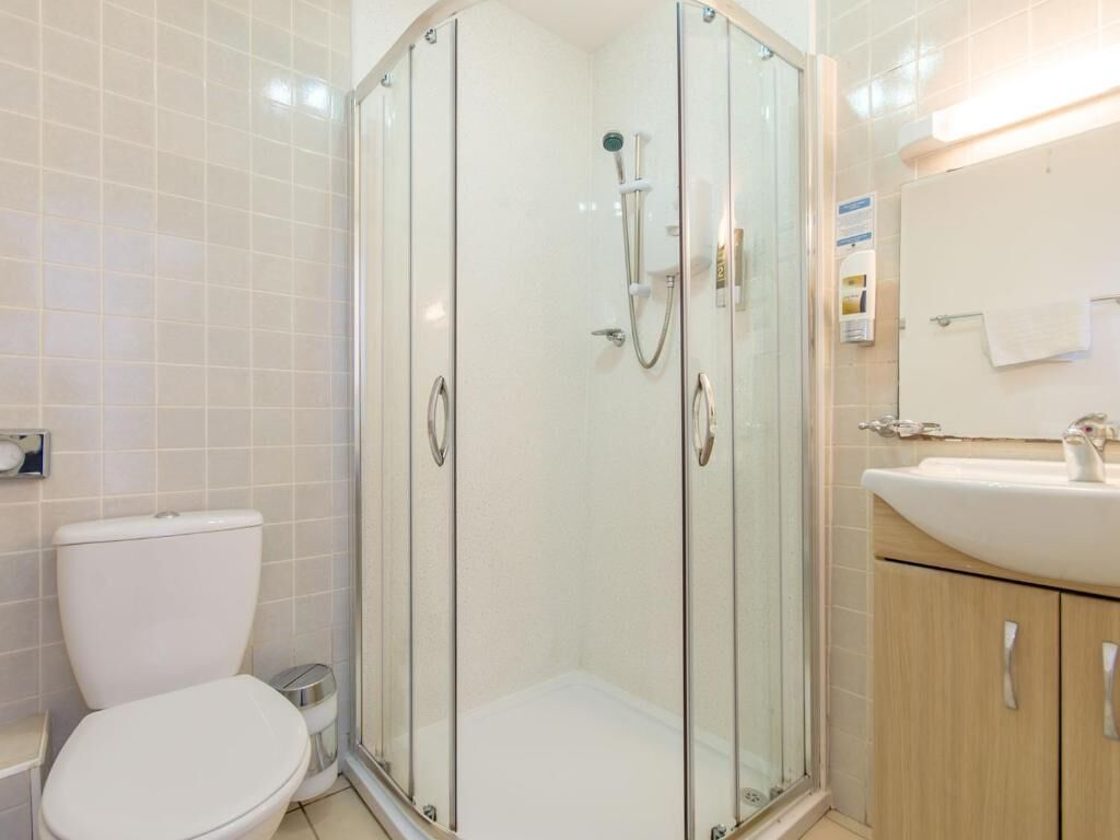 A modern bathroom with a glass-enclosed shower, a toilet, and a sink with a mirror.
