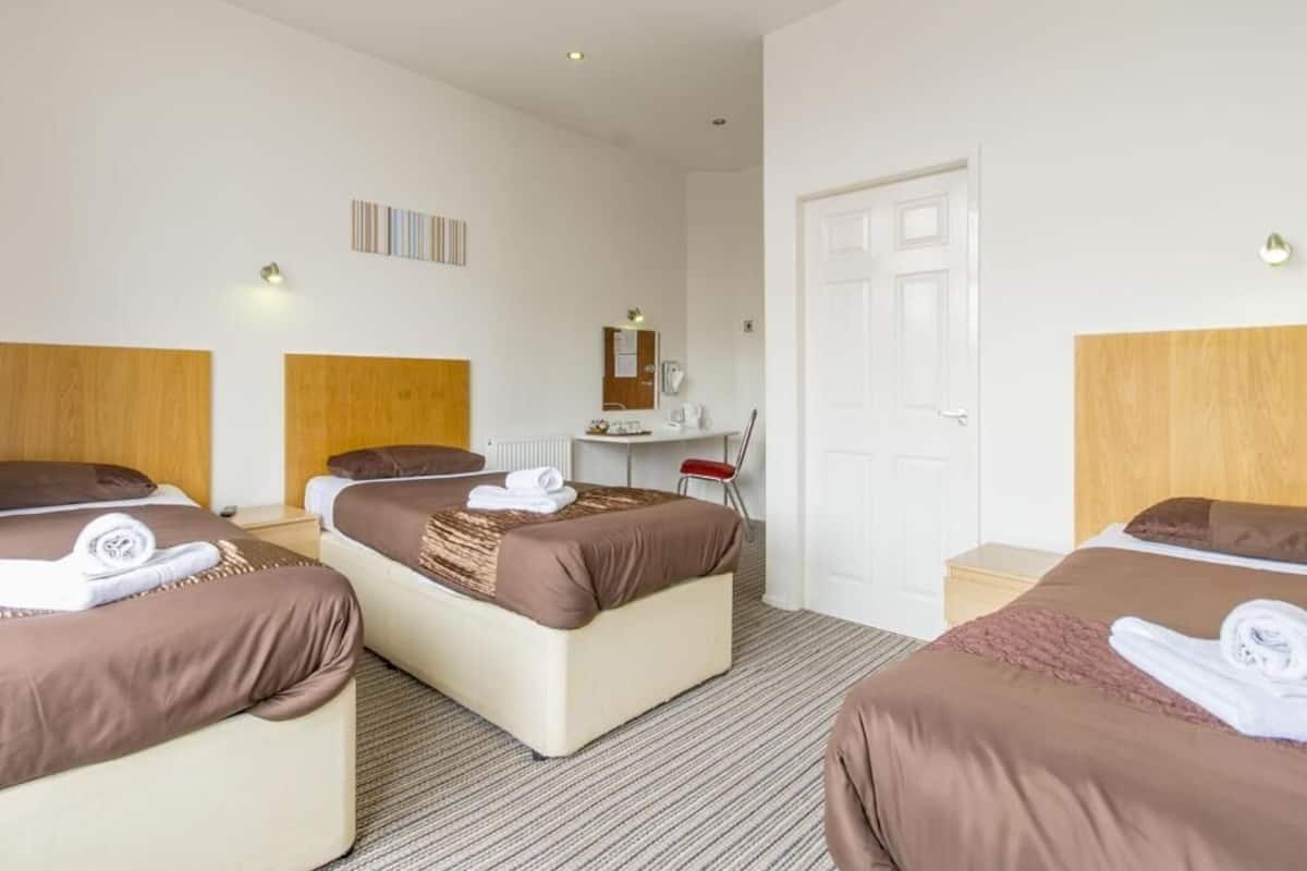 A hotel room with three beds, a desk, a chair, and a mirror.