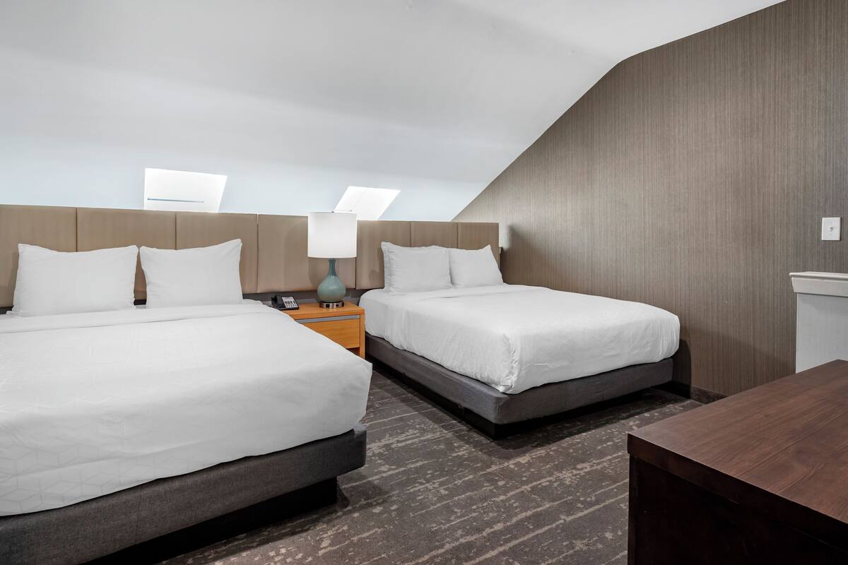 Une chambre d’hôtel avec deux lits, un bureau, une table de chevet et une lampe.