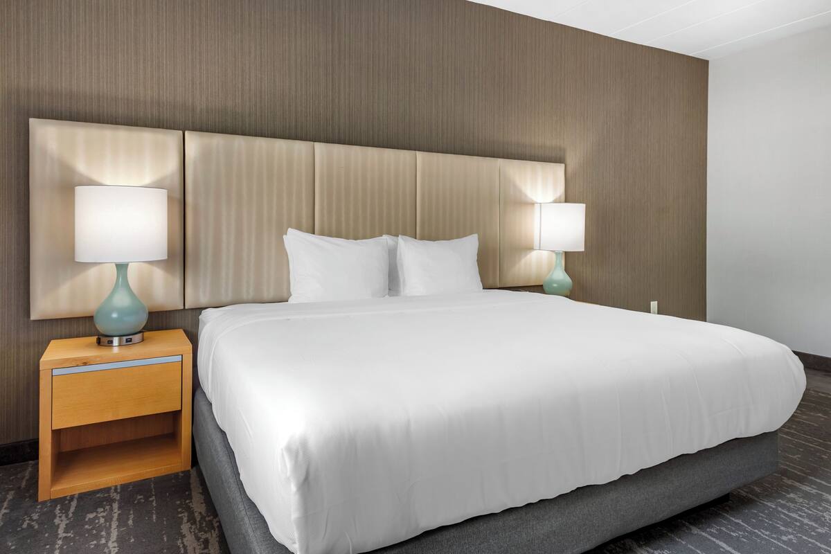 Une chambre d’hôtel avec un grand lit, deux tables de chevet avec des lampes et une tête de lit dotée d’un éclairage intégré.