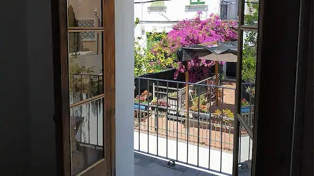 An open door leading to a balcony with a view of a building and pink flowers.