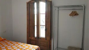 A room with two beds covered in orange floral bedding, a wooden door, a metal wardrobe, and a hanging light fixture.
