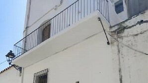 A white building with a wooden door and a window with a metal grille.