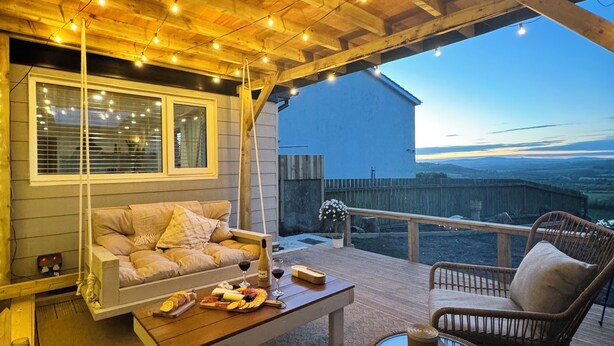 An outdoor seating area with a wooden ceiling, string lights, a sofa, a table with food and drinks, and a view of the landscape. - Kennel House with Hill Views perfectly situated for walks. - 20 min to the beach (Whitland)