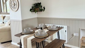 A dining area with a wooden table set for four, a hanging light fixture, and two wall-mounted shelves with plants. - Kennel House with Hill Views perfectly situated for walks. - 20 min to the beach (Whitland)