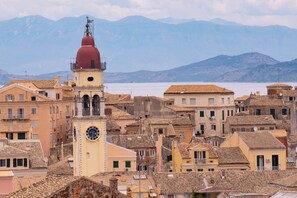 Un pueblo costero con edificios históricos, una imponente torre del reloj y montañas al fondo.