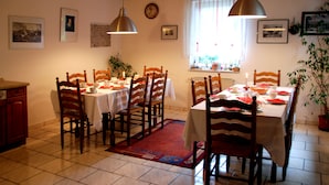 A dining area with wooden chairs and tables, a clock on the wall, and a window with curtains. - Landhaus (Lützen)