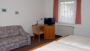 A hotel room with a bed, a desk with a computer, a chair, a sofa, and a window with curtains. - Landhaus (Lützen)