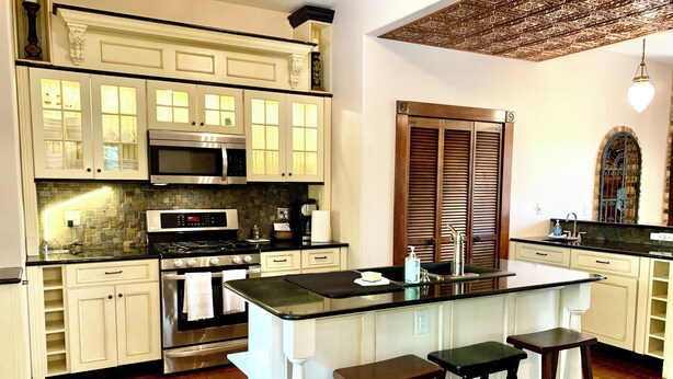 Una cocina con gabinetes blancos, estufa de acero inoxidable, microondas e isla de madera con taburetes.