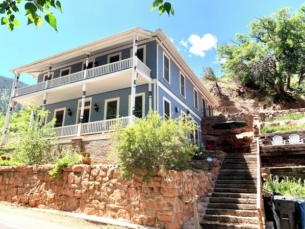 Una casa de dos pisos con un balcón, escalones de piedra y vistas del paisaje circundante.