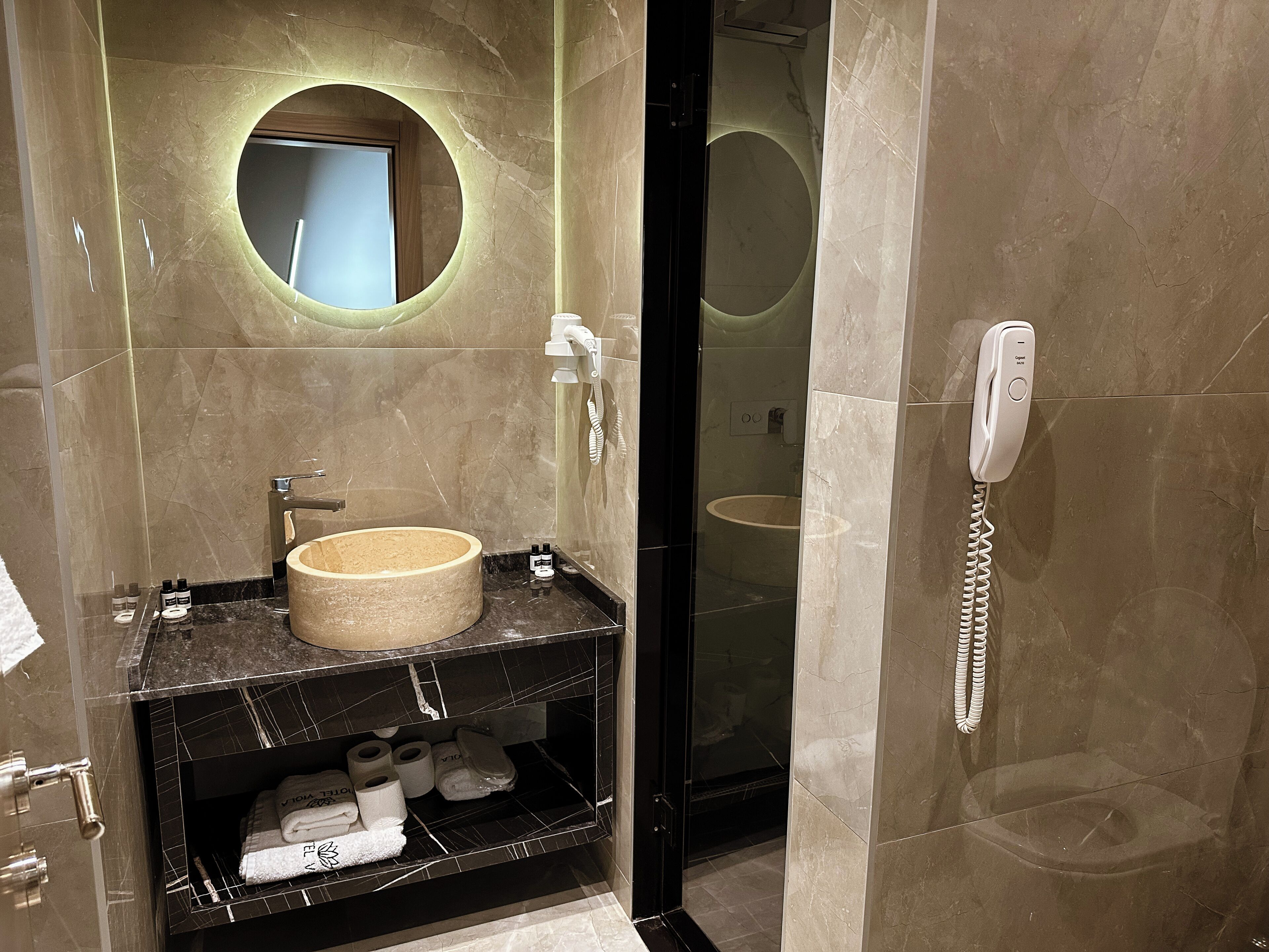 Een badkamer met een marmeren wastafel, een spiegel, een douche met glazen wanden en een telefoon.