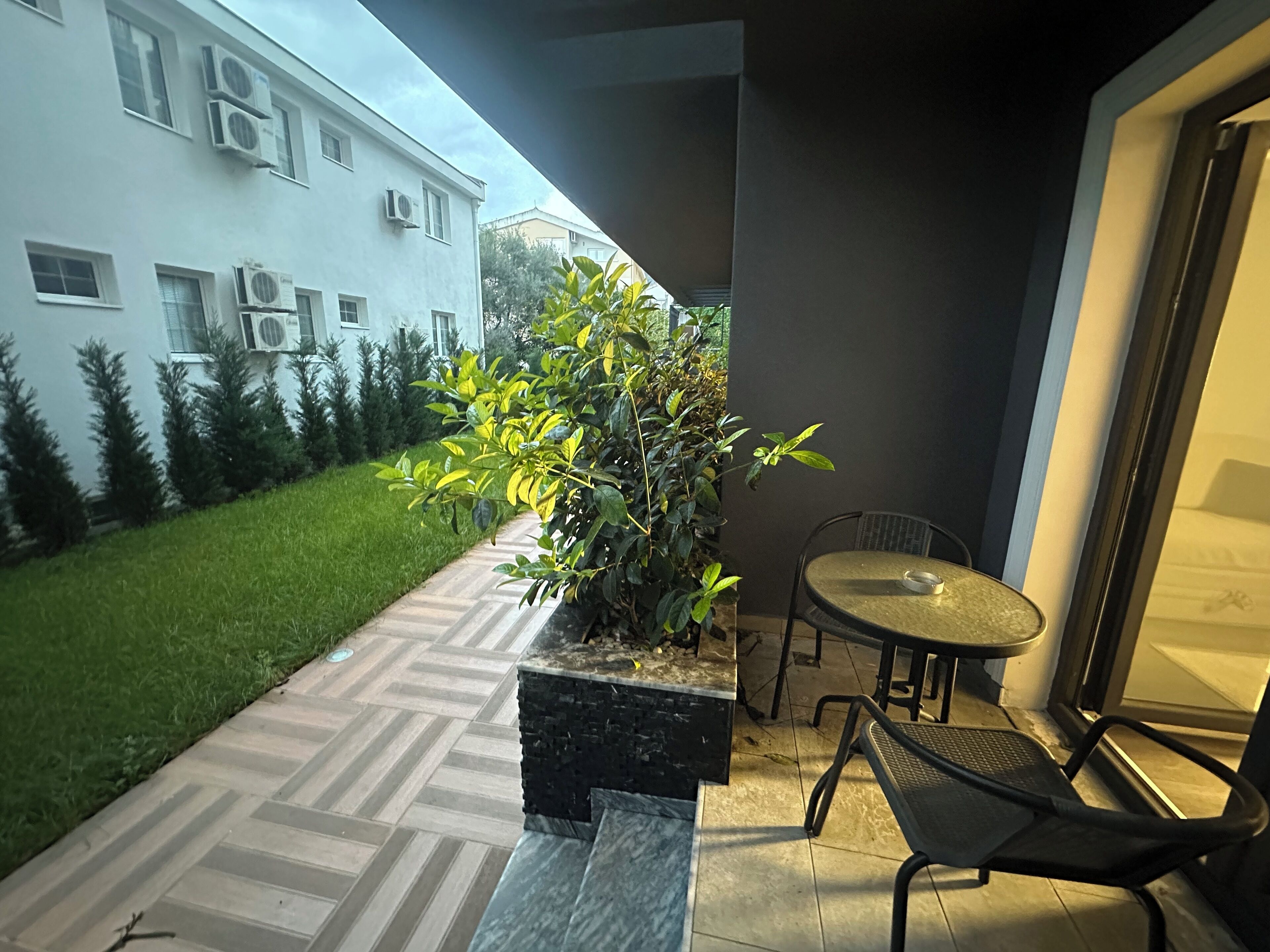 A patio with a table and chairs, a potted plant, and a view of a white building with air conditioning units.