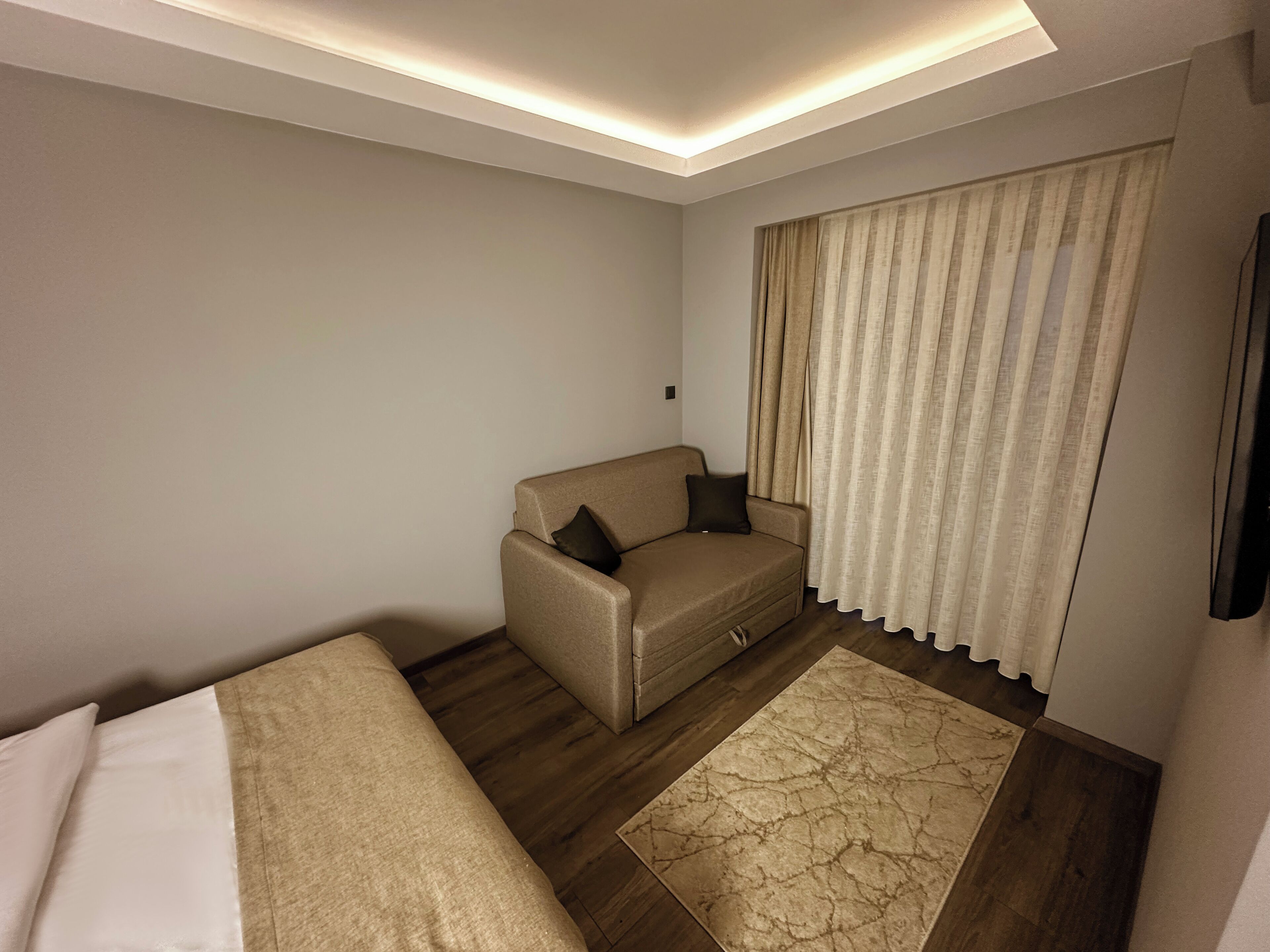 Une chambre d’hôtel moderne, dotée d’un canapé, d’un petit tapis et d’une grande fenêtre avec des rideaux.