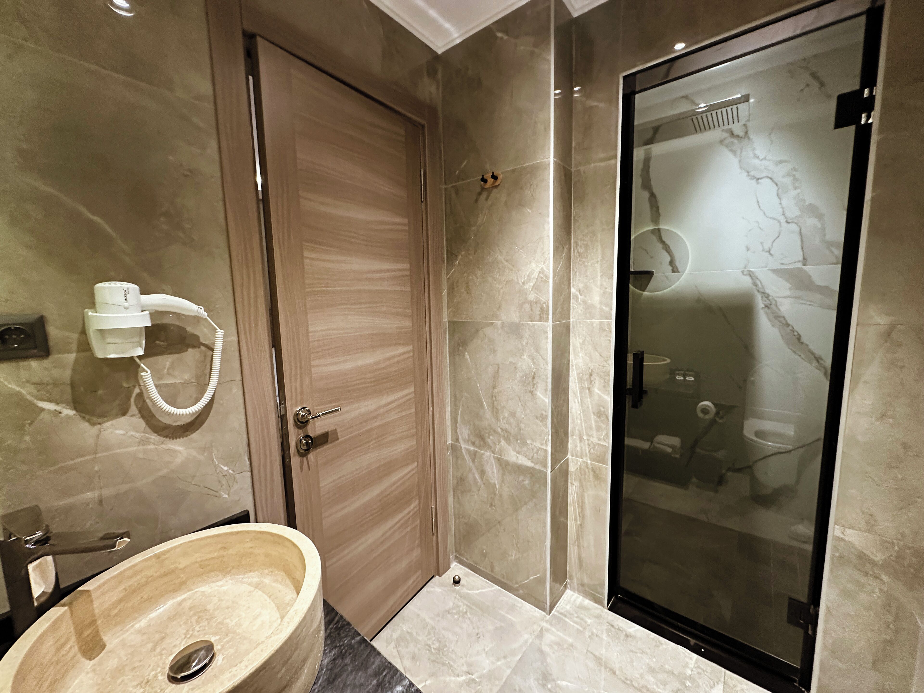 A modern bathroom with a marble sink, a glass-enclosed shower, and a hairdryer on the wall.