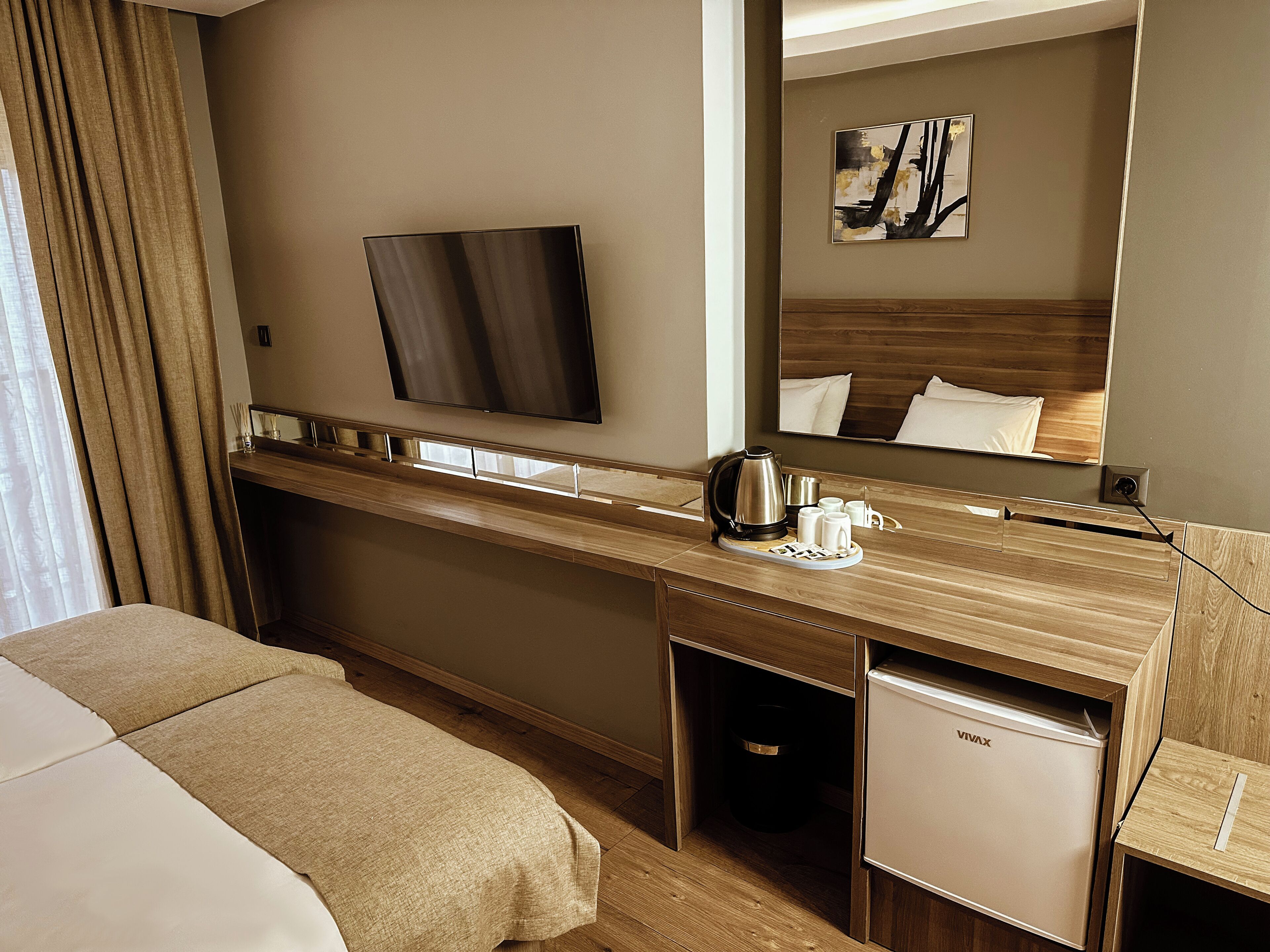 A hotel room with a bed, a desk with a coffee maker, a mini fridge, and a large mirror.