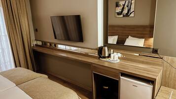 Een hotelkamer met een bed, een bureau met een koffiezetapparaat, een minibar en een grote spiegel.