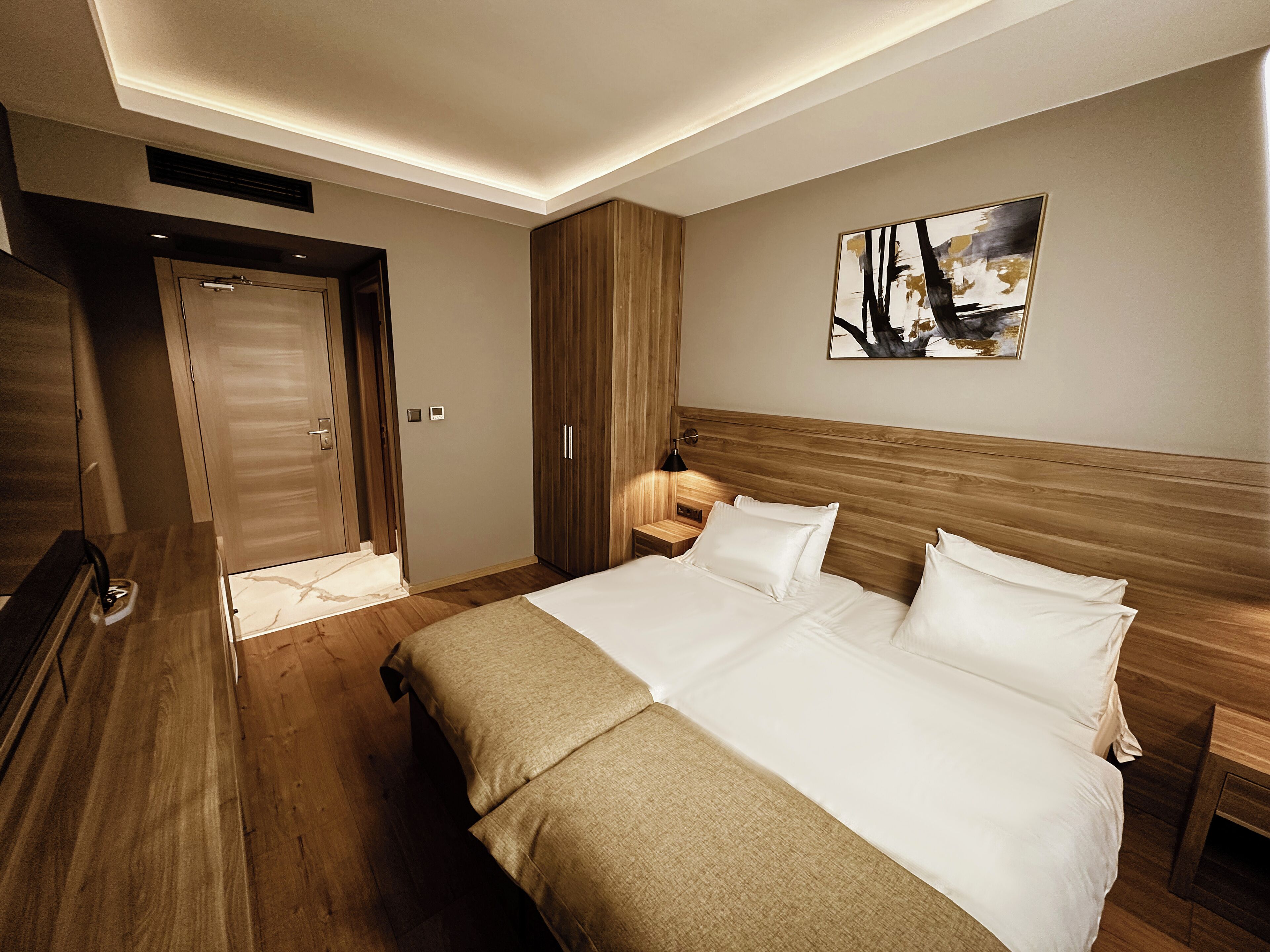 Habitación de hotel con una cama grande, cabecera de madera, una mesita de noche, una lámpara y un armario.