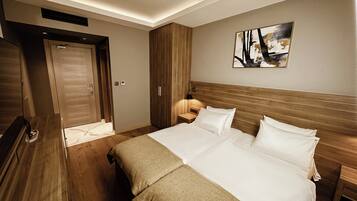 Habitación de hotel con una cama grande, cabecera de madera, una mesita de noche, una lámpara y un armario.