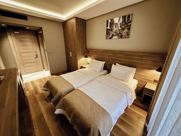 Habitación de hotel con dos camas, piso de madera, un armario, un cuadro en la pared y un escritorio con lámpara.