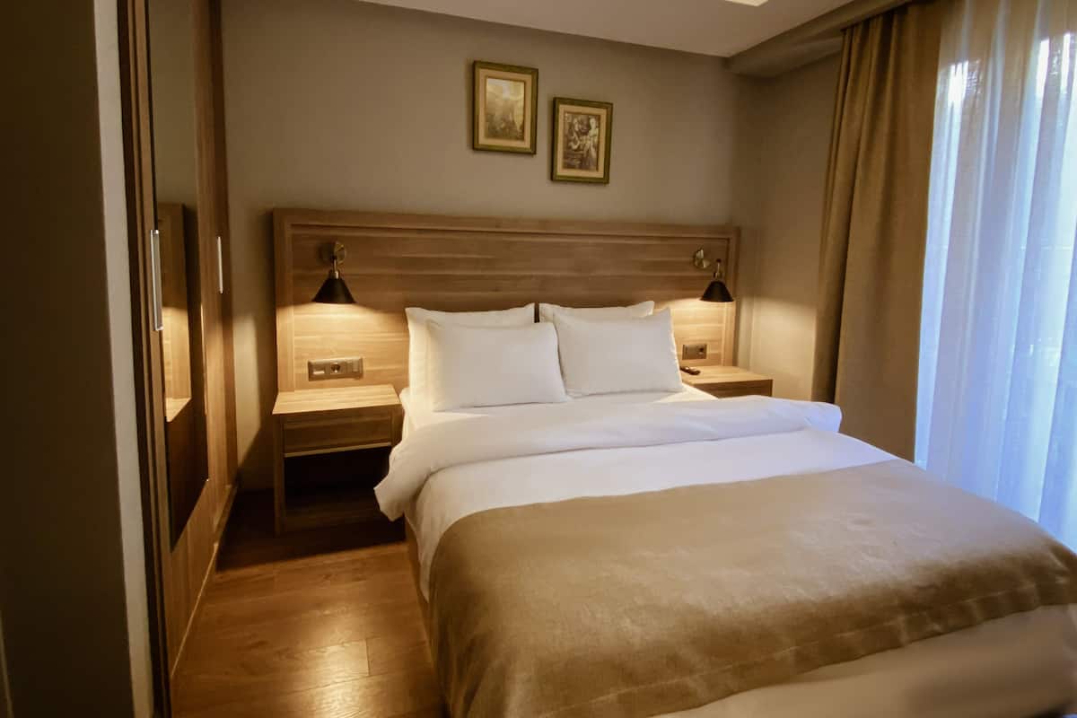 Une chambre d’hôtel avec un grand lit, deux tables de chevet avec des lampes, une tête de lit en bois et deux tableaux encadrés au mur.