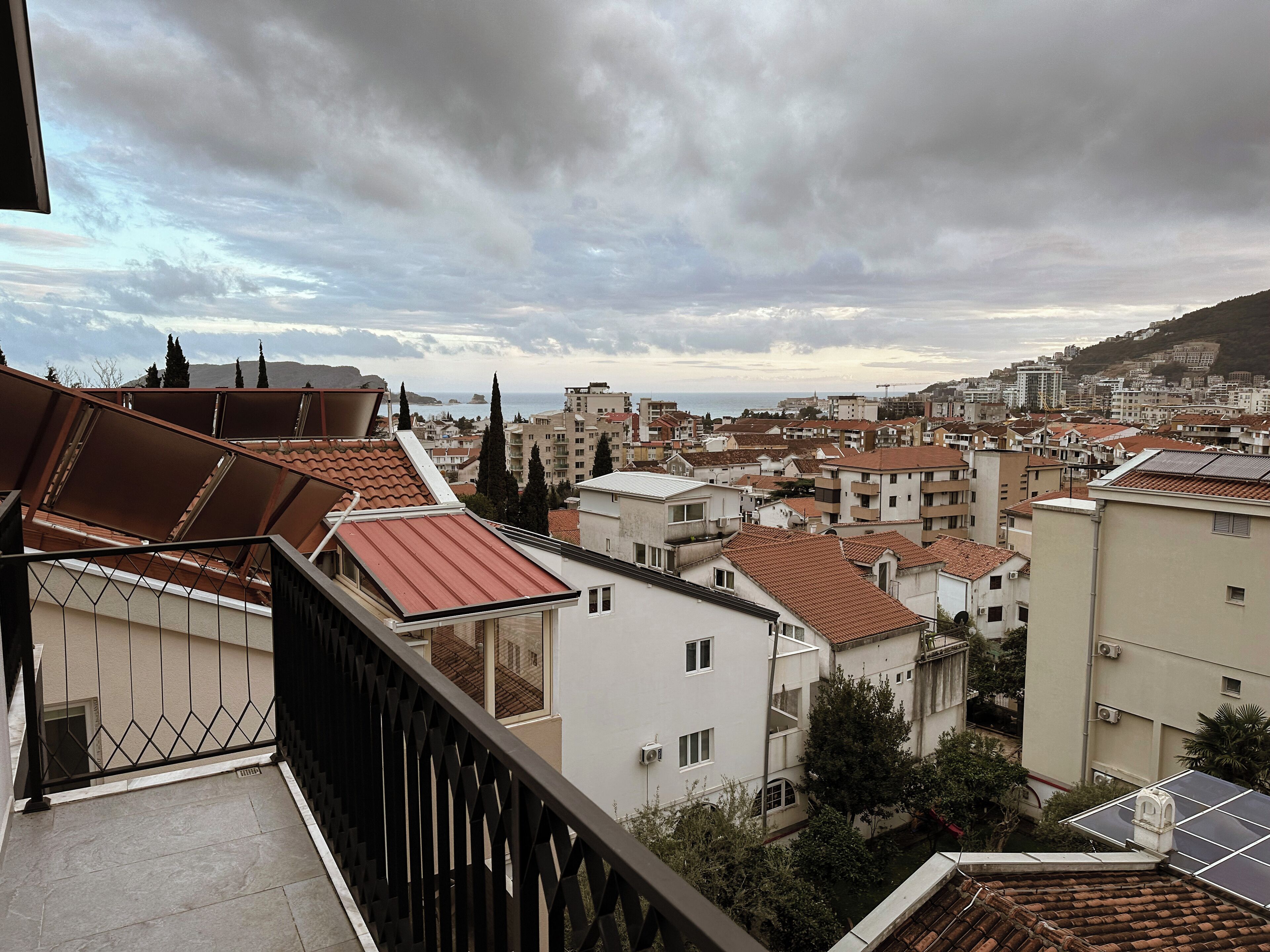 Zona residencial con tejados de tejas rojas, una mezcla de alturas de edificios y una vista distante del mar bajo un cielo nublado.