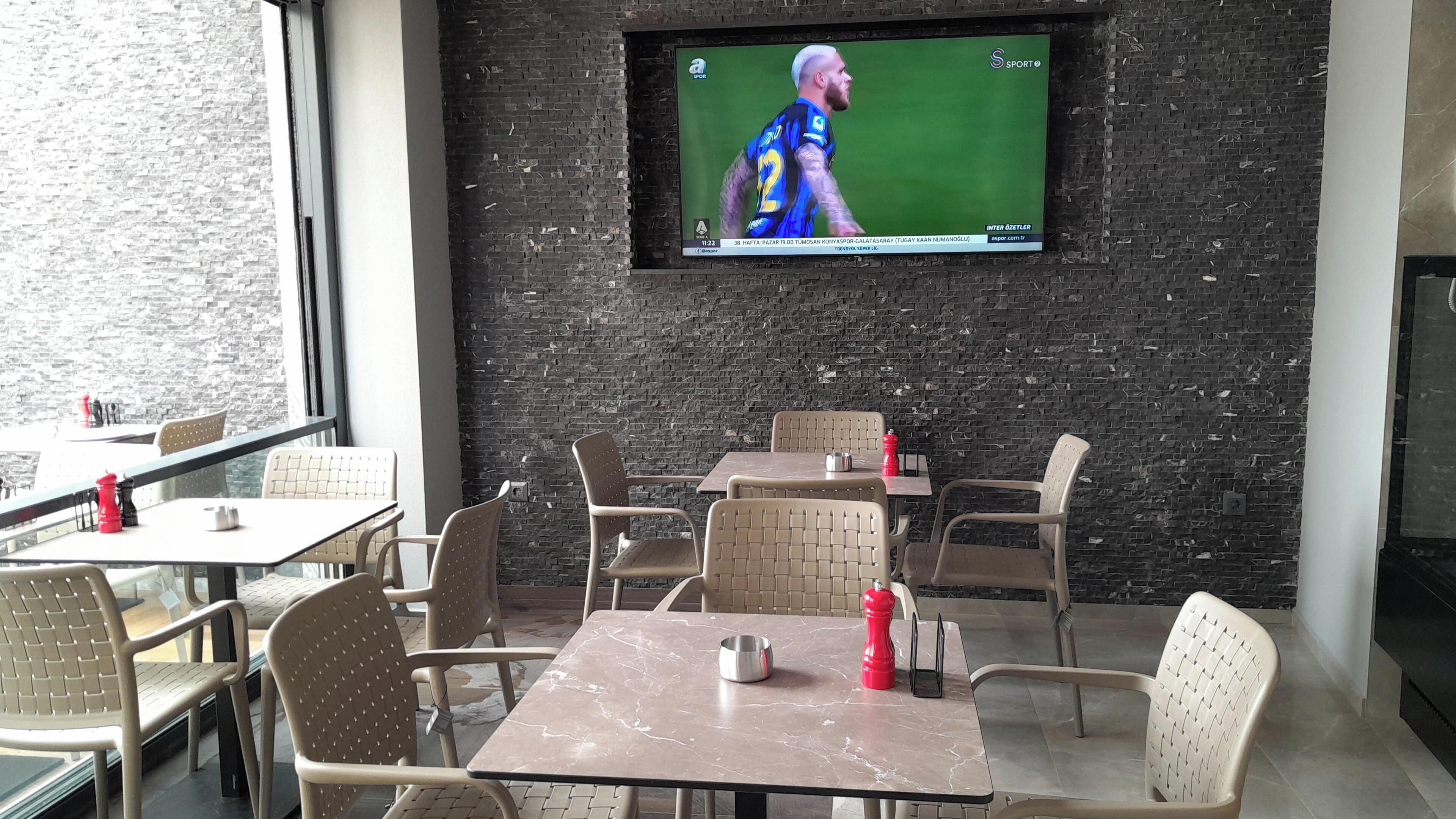 En restaurant med udendørs siddepladser, en murstensvæg og et fjernsyn, der viser en sportsbegivenhed.