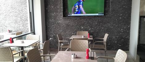 En restaurant med udendørs siddepladser, en murstensvæg og et fjernsyn, der viser en sportsbegivenhed.