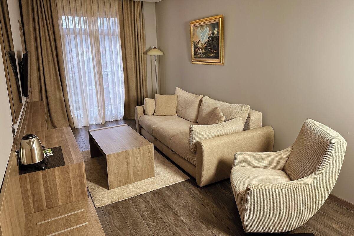 Un salon moderne avec un canapé, une table basse et un fauteuil. Un tableau est accroché au mur et une lampe se trouve à côté du canapé.