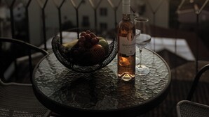 A table with a bottle of wine, a glass, and a fruit basket on a balcony overlooking a mountain at sunset. - Viola Hotel Budva (Budva)
