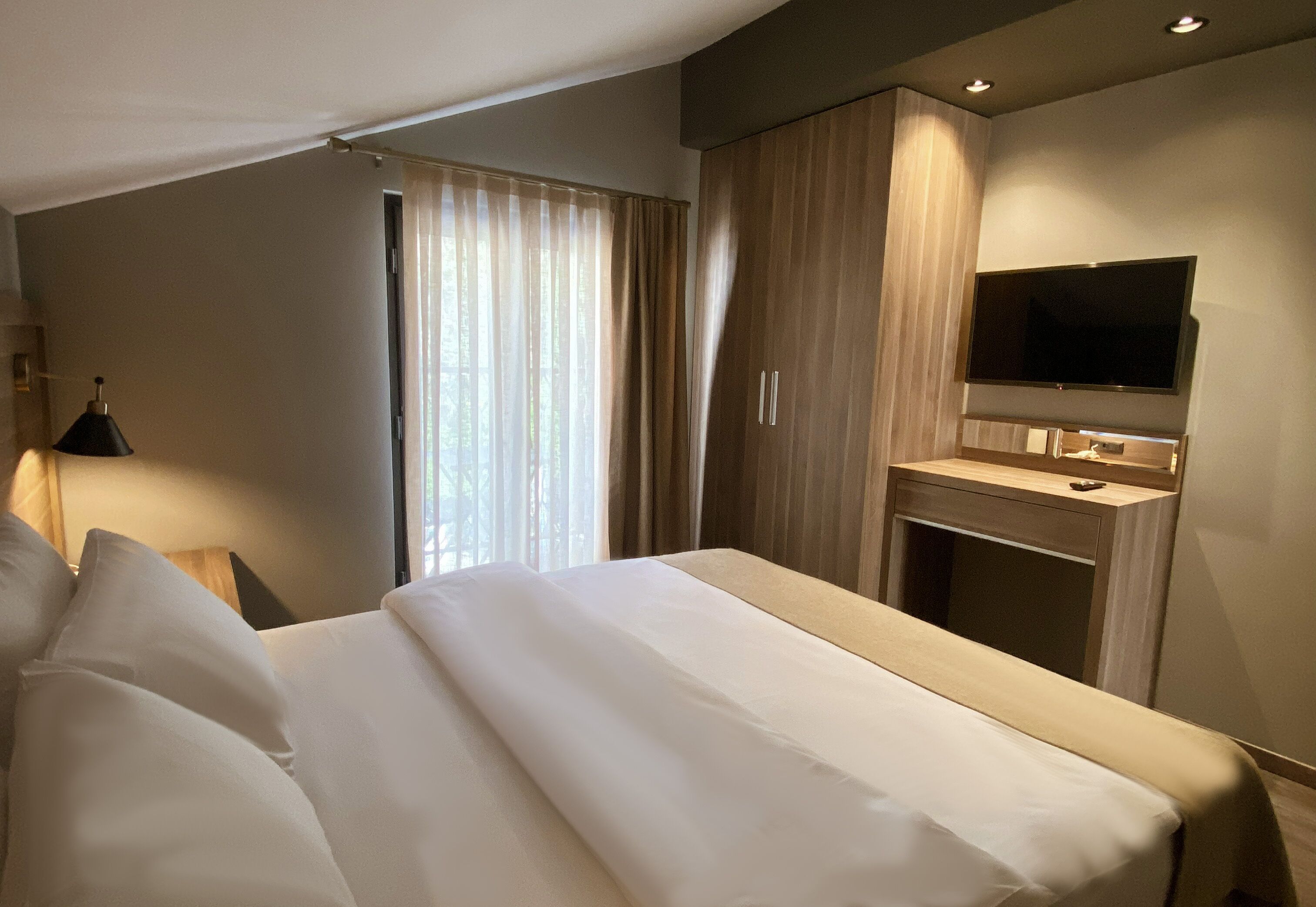 A hotel room with a bed, a desk, a TV, and a window with curtains.