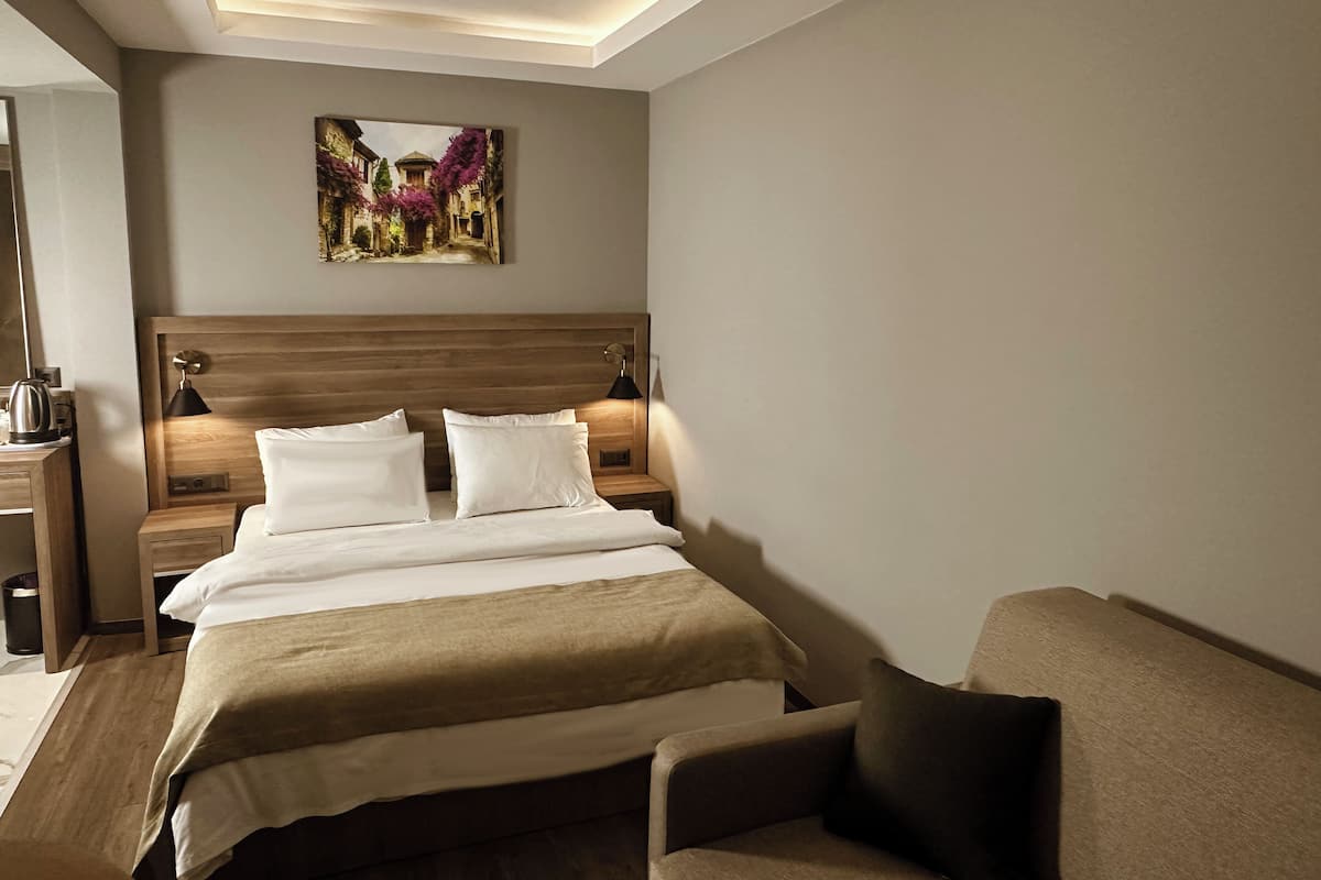 Une chambre d’hôtel avec une tête de lit en bois, un lit recouvert de draps blancs, une table de chevet avec une lampe et un tableau accroché au mur.