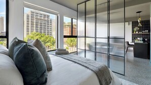 A modern bedroom with a large bed, a sliding glass door to a balcony, and a view of city buildings. - Modern City Escape with Rooftop Pool Views (Cape Town)